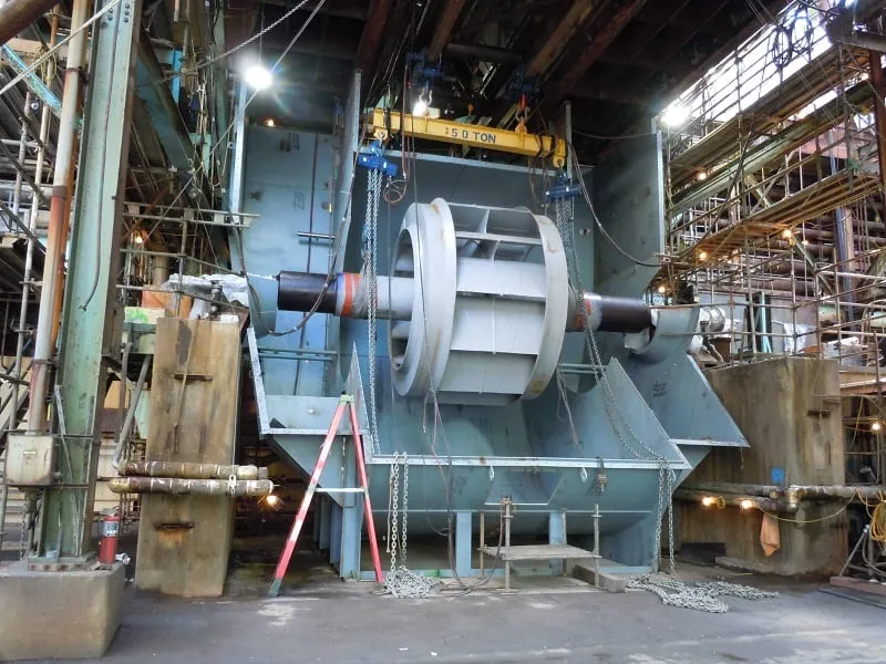 A large fan rotor rigged beneath a 50-ton overhead crane on a fabrication floor