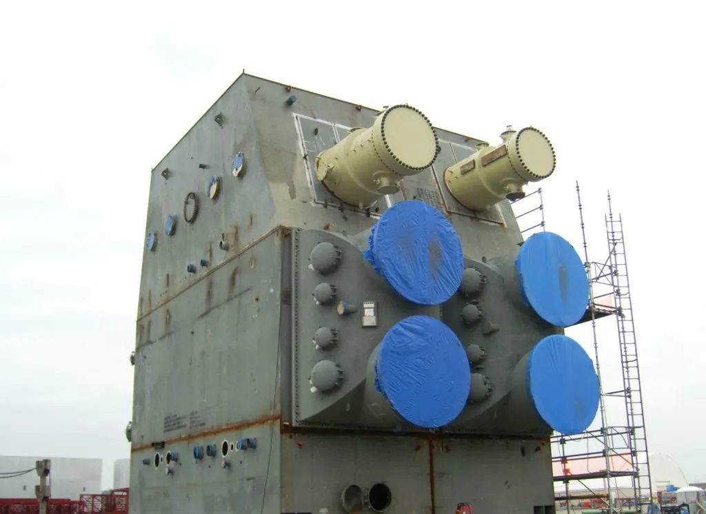 A steam condenser unit on site, wrapped for shipment with scaffolding alongside