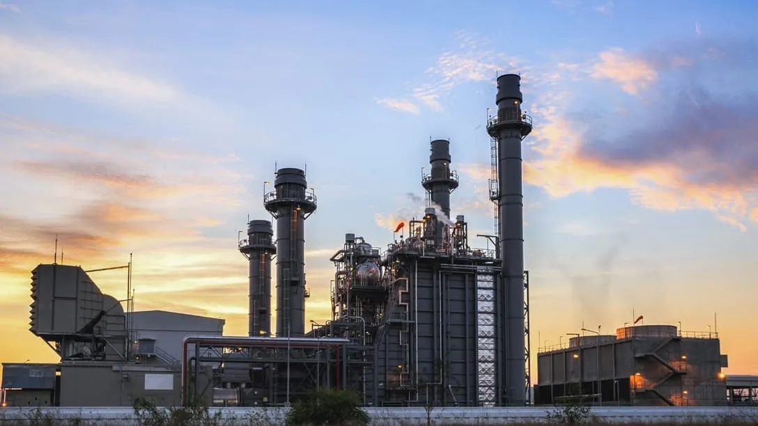 A combined-cycle power plant at dusk, its stacks, heat-recovery units and cooling tower cells lit against the sky