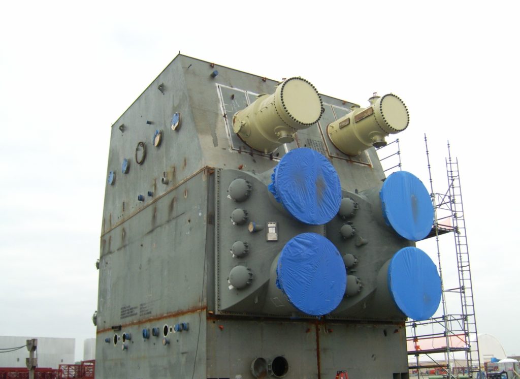 A steam condenser unit on site, wrapped for shipment with scaffolding alongside